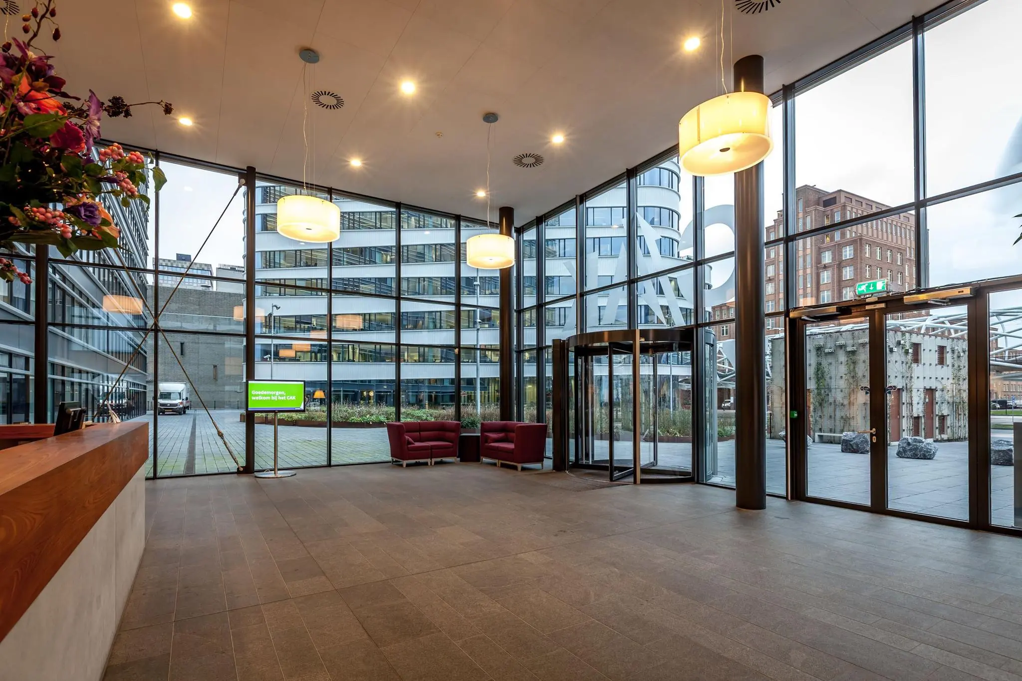 Moderne entreehal van een kantoorpand aan de Prinses Beatrixlaan met glazen gevel, zitgedeelte en automatische draaideur.